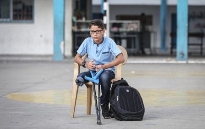 World Health Organization photo of a Palestinian youth amputee with crutches. He is wearing glasses, a blue top and jeans.