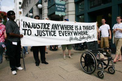 A wheelchairs with Justin Dart's hat on the seat is in front of a sign with a quote from Dr. Martin Luther King Jr.